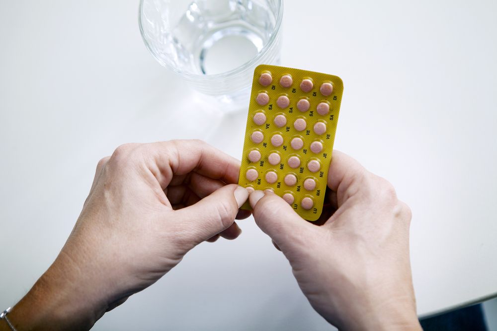 Hands holding a blister pack of tablets beside a glass of water